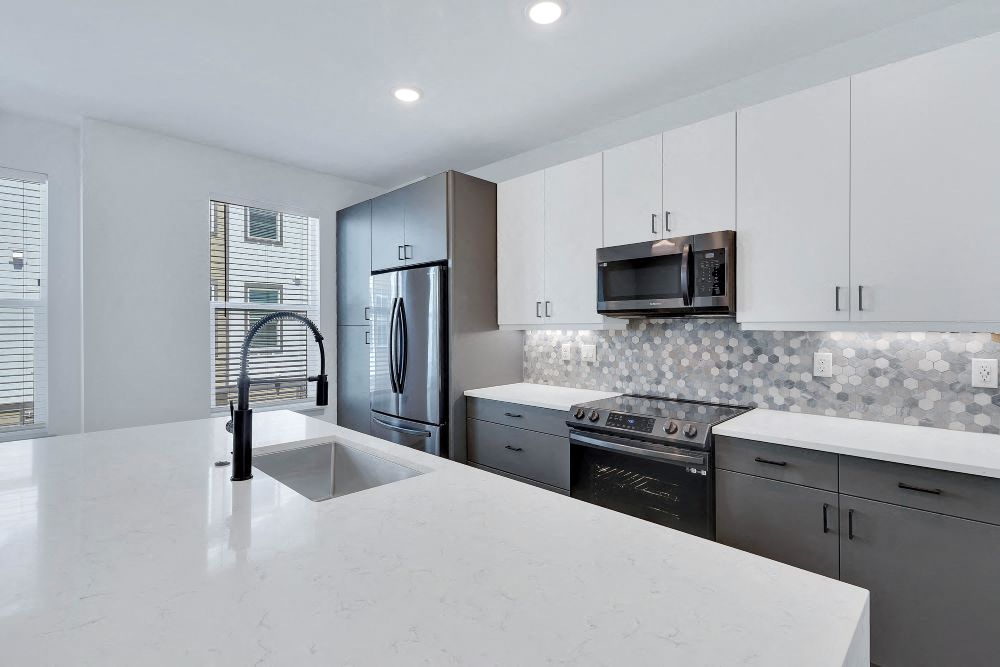 View of kitchen with large waterfall island and sink, tile backsplash, soft closing cabinets and black stainless steel appliances